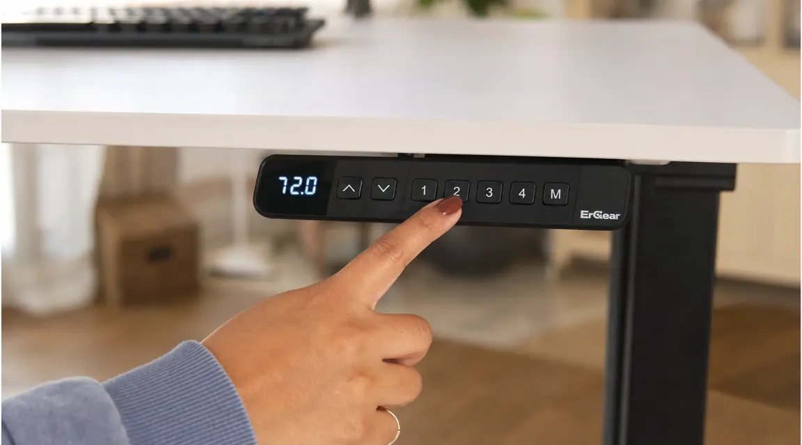 Close-up of a finger pressing a preset button on a standing desk control panel mounted to the desk frame